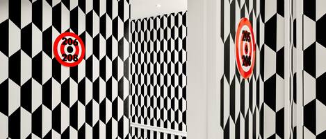 Un couloir avec un mur orné d’un motif géométrique en noir et blanc et une rambarde blanche.