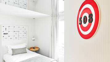 A hotel room with a bed, a bedside table, a wall with a target sign, and a window with curtains.