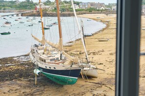 A boat moored on a sandy beach with a backdrop of houses and a bridge. - The Atlantic (Isles of Scilly)