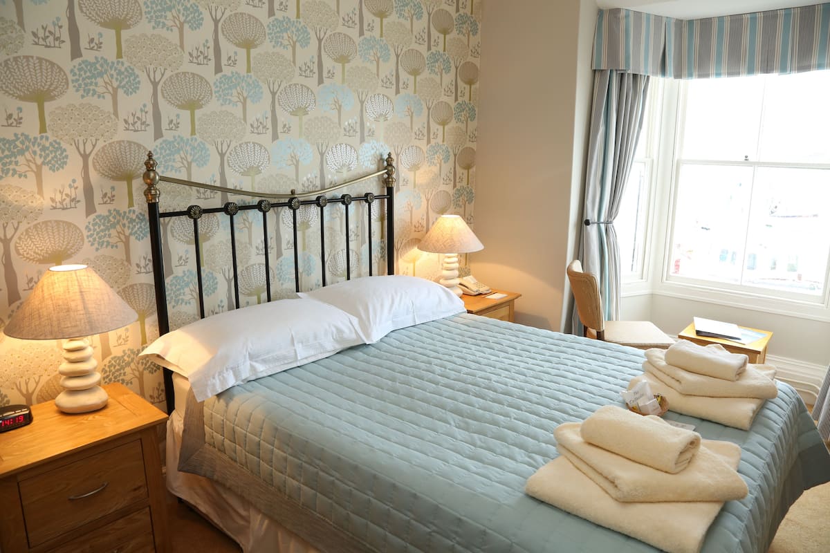 A neatly made bed with a blue quilt, two bedside lamps, and a nightstand with a clock.
