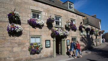 Traditional stone building with a flat roof and evenly spaced windows, featuring hanging flower baskets and an accessible entrance.