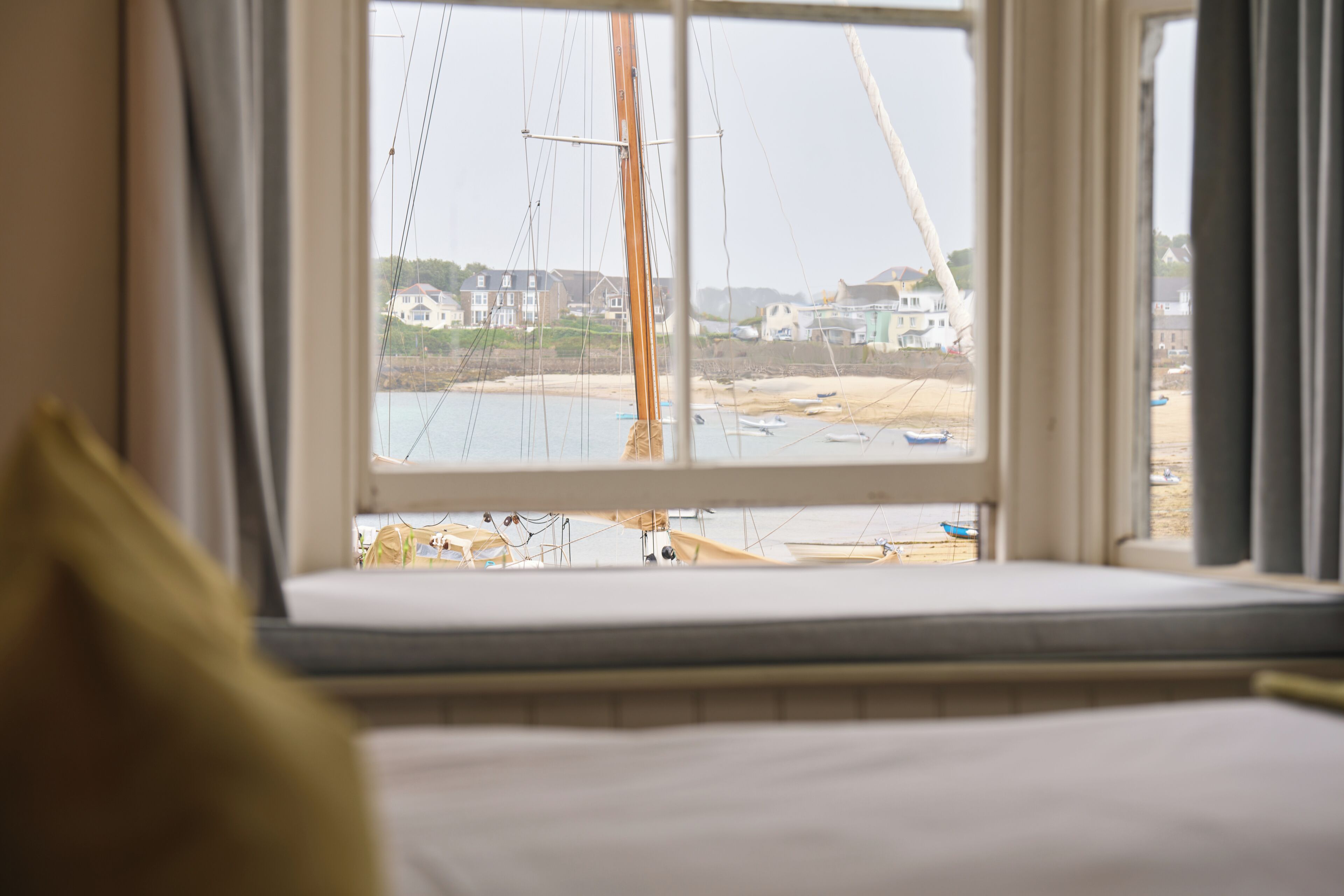 A bed with a view of a coastal area through a window, including boats and buildings.