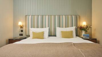A hotel room with a large bed, two bedside lamps, a nightstand with a vase of flowers, and a striped headboard.