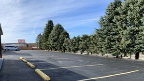 Un parking avec des places délimitées et des bordures jaunes, entouré d’arbres et d’un bâtiment sur lequel est apposée une enseigne.