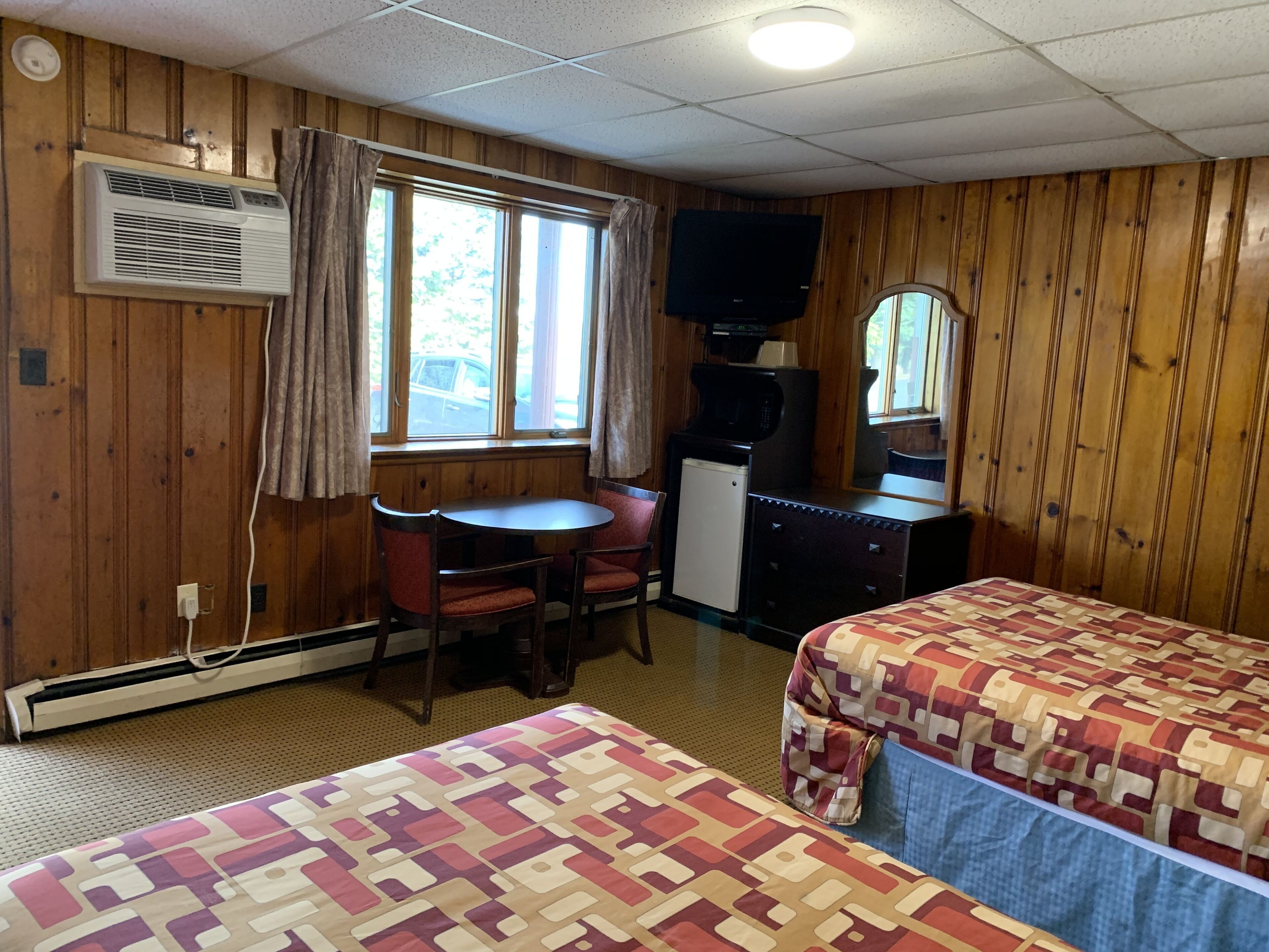 A motel room with two beds, a small desk, a television, and a window with curtains.