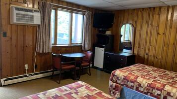 A motel room with two beds, a small desk, a television, and a window with curtains.