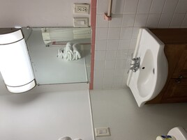 Un baño con lavamanos blanco, espejo y toallero.