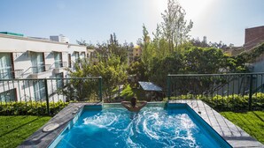 Piscina con una persona nadando, rodeada de vegetación y edificios.