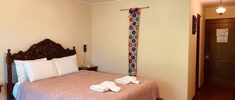 A bedroom with a wooden bed, a bedside table with a lamp, a hanging floral curtain, and a door with a lock.