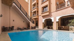 An indoor swimming pool with lounge chairs and tables, surrounded by a multi-story building with balconies. - Riad Marrakech House (Marrakech)