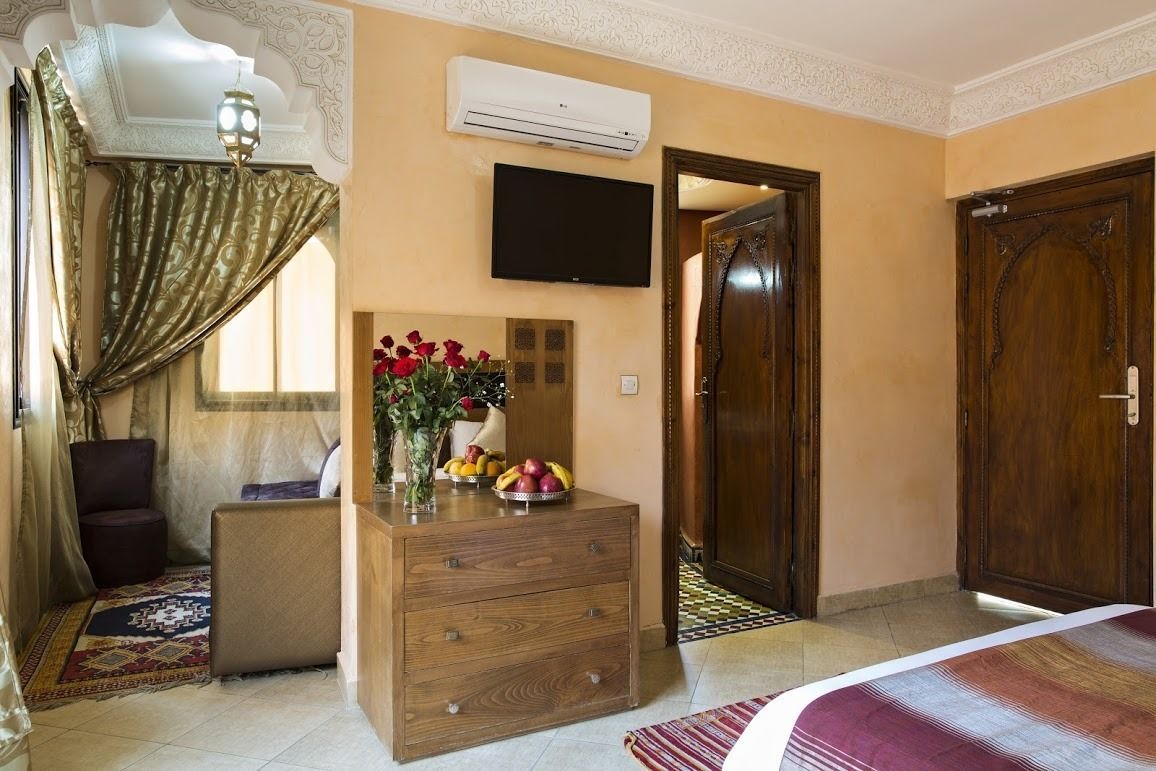 Quarto de hotel com cómoda de madeira, televisão de ecrã plano na parede e uma porta de madeira grande.