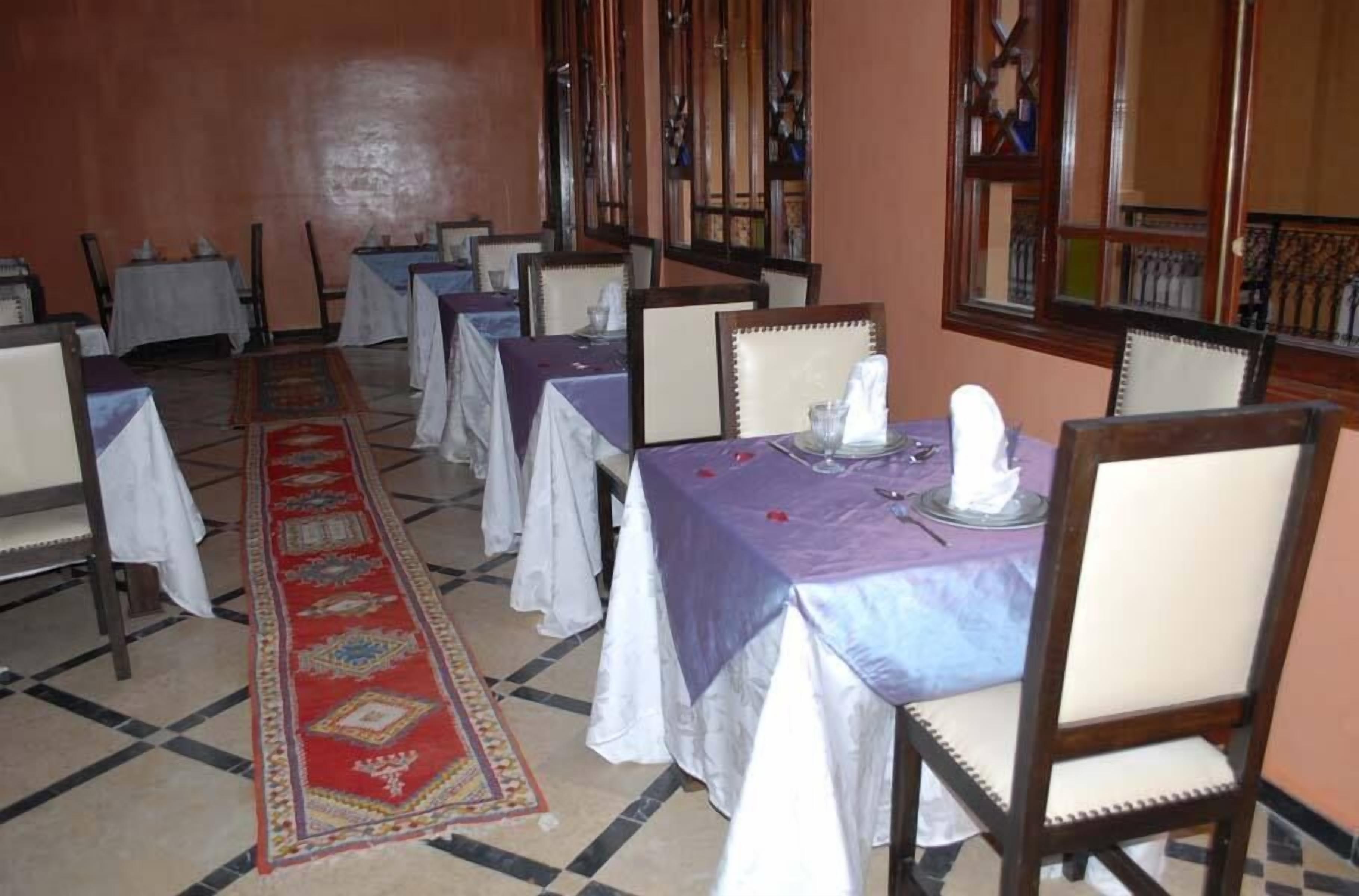 Un comedor con mesas dispuestas para el servicio, una alfombra estampada y un ventanal con vidrieras.