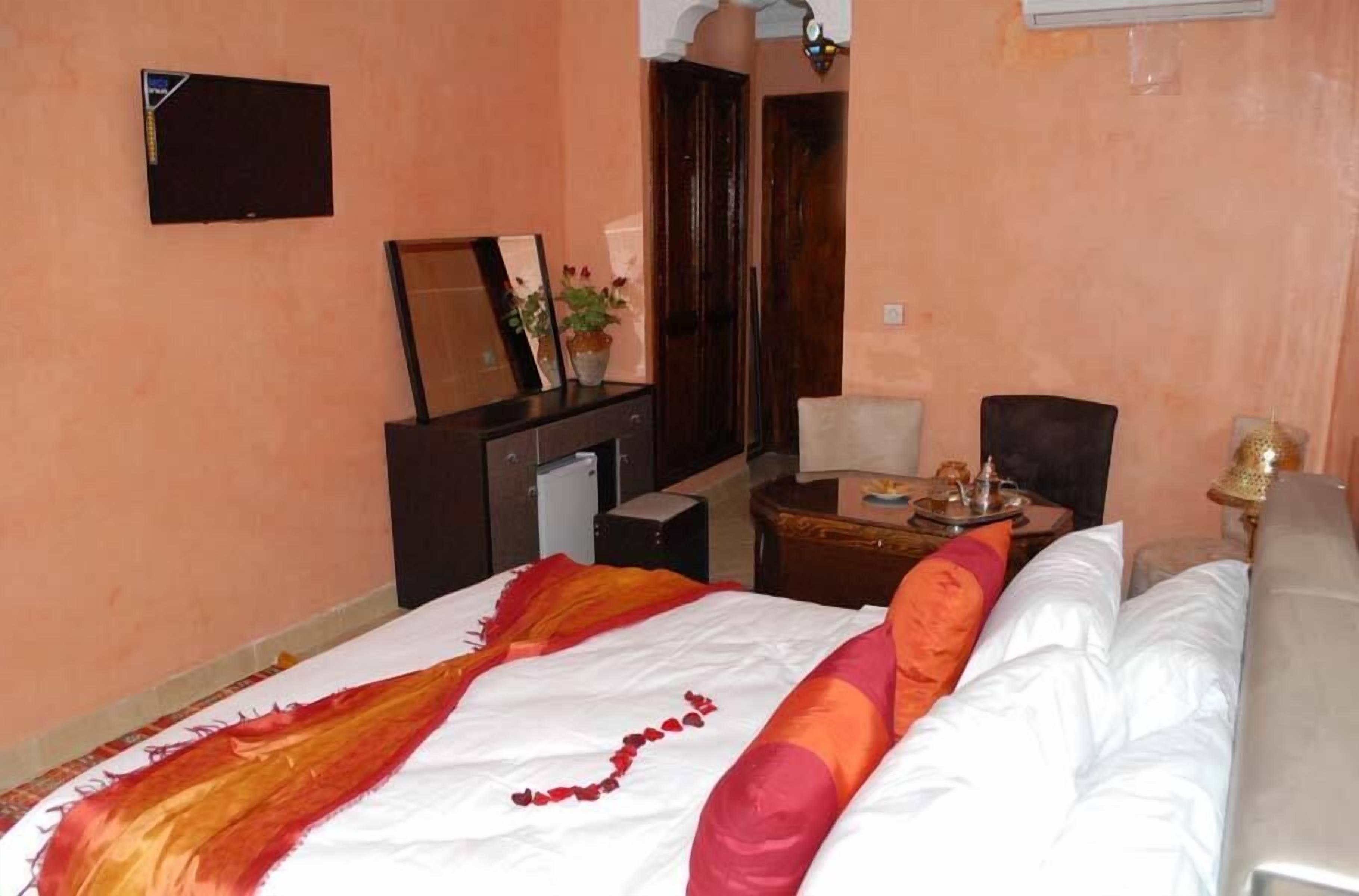 A hotel room with a bed, a desk, a chair, a television, and a door.