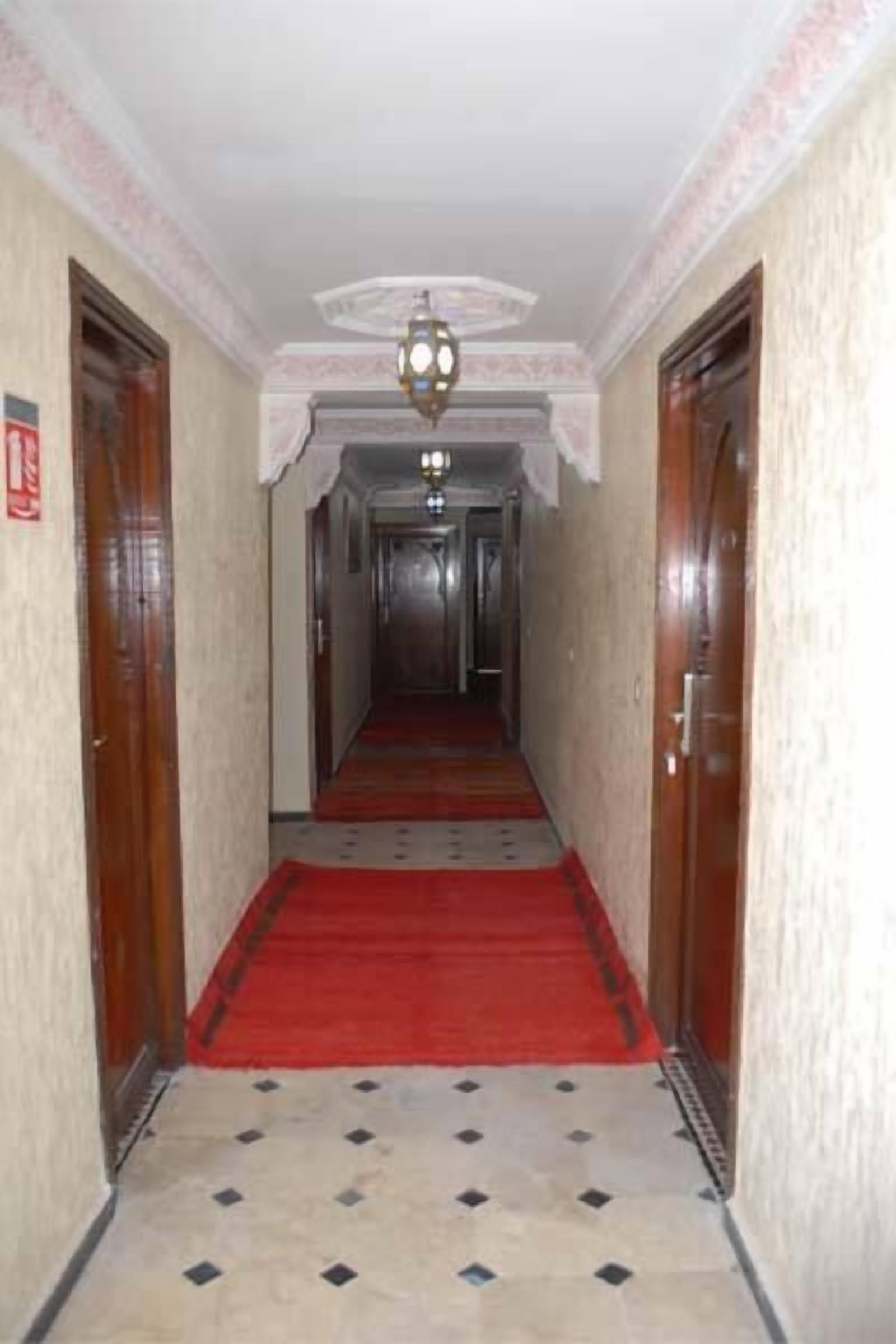 A hallway with a red carpet, tiled floor, and wooden doors.