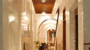 A corridor with a wooden ceiling, a hanging light fixture, and patterned rugs. - Riad Marrakech House (Marrakech)