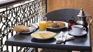 A balcony table with breakfast items including bread, a plate of flatbreads, a glass of orange juice, and a cup of coffee. - Riad Marrakech House (Marrakech)