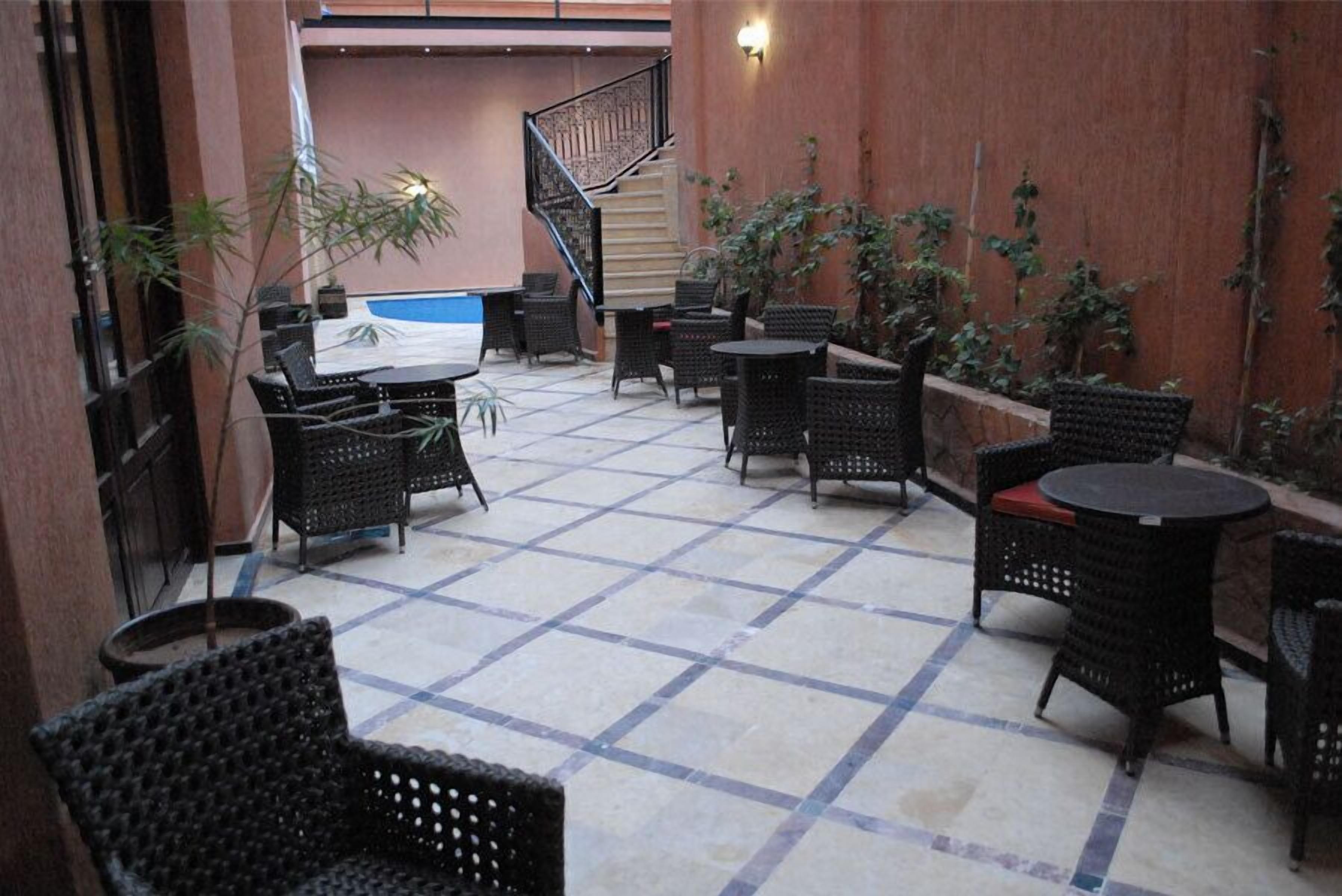An outdoor patio area with tiled flooring, black wicker furniture, and potted plants.