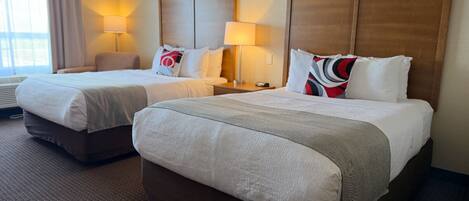 A hotel room with two beds, each with a wooden headboard, a bedside table, and a lamp.