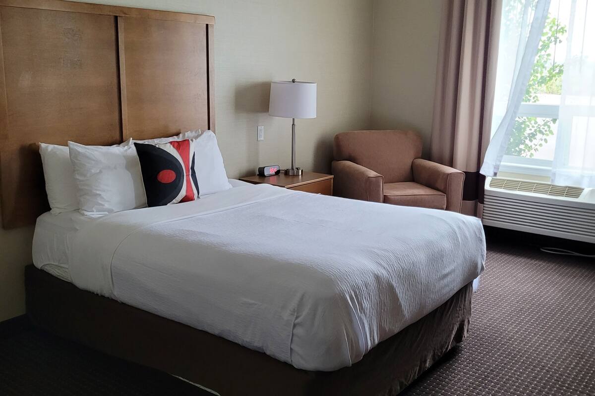 Une chambre d’hôtel avec un grand lit, une chaise, une lampe et une fenêtre avec des rideaux.