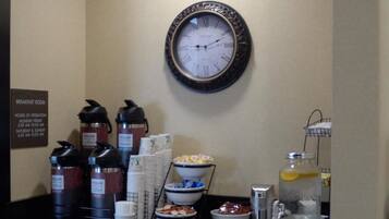 Un coin petit-déjeuner avec des distributeurs de café, des bols remplis de nourriture et une horloge au mur.