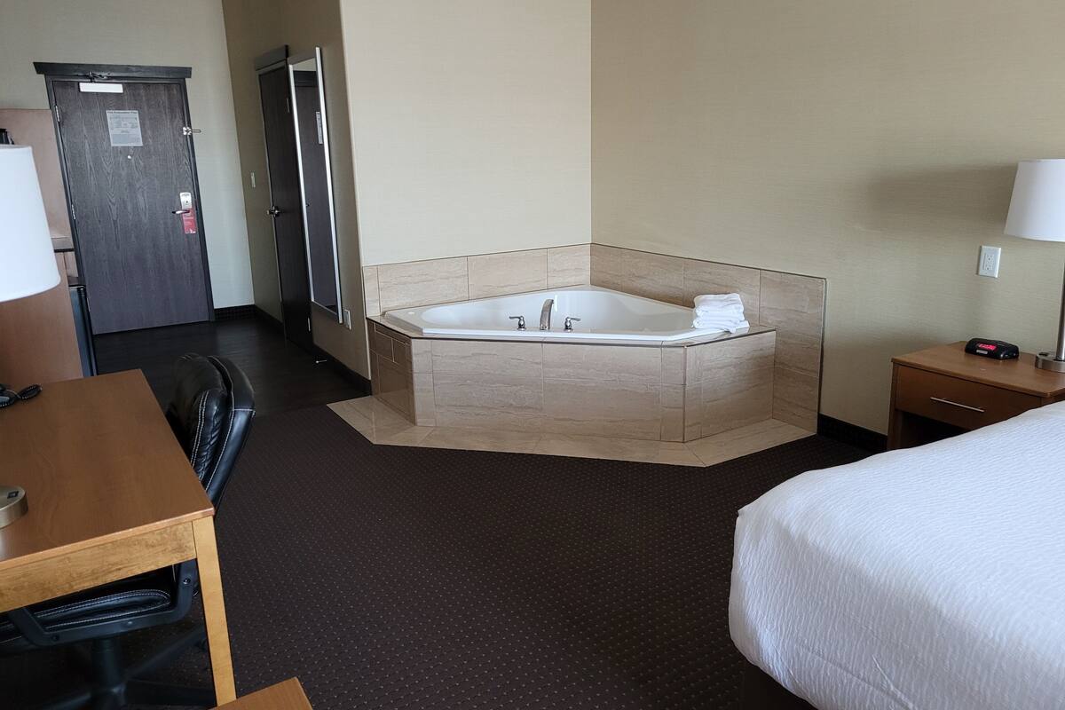 Une chambre d’hôtel avec une grande baignoire, un bureau, une chaise, un lit et une petite table avec une lampe.