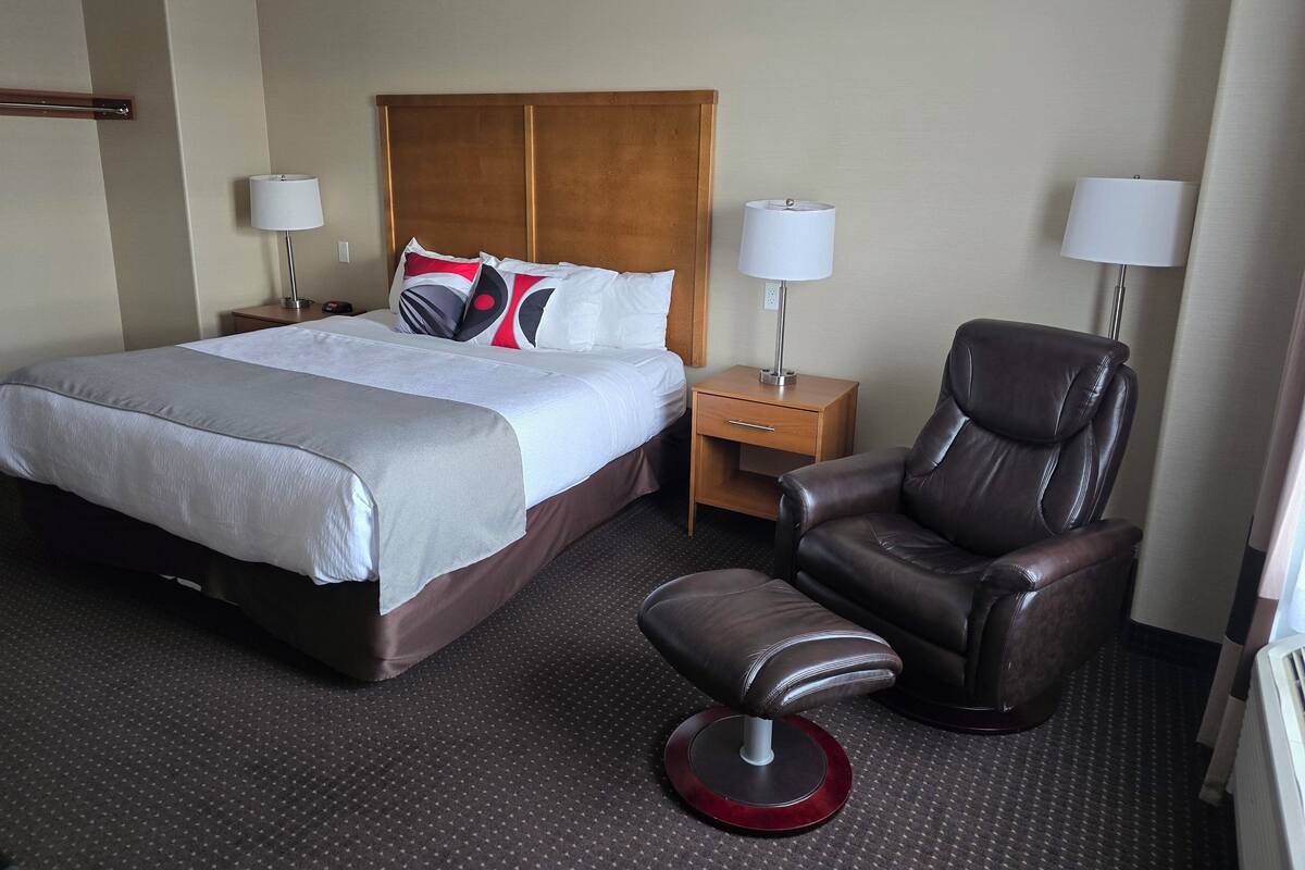 Une chambre d’hôtel avec un grand lit, deux tables de chevet avec des lampes, un fauteuil en cuir et un repose-pieds.