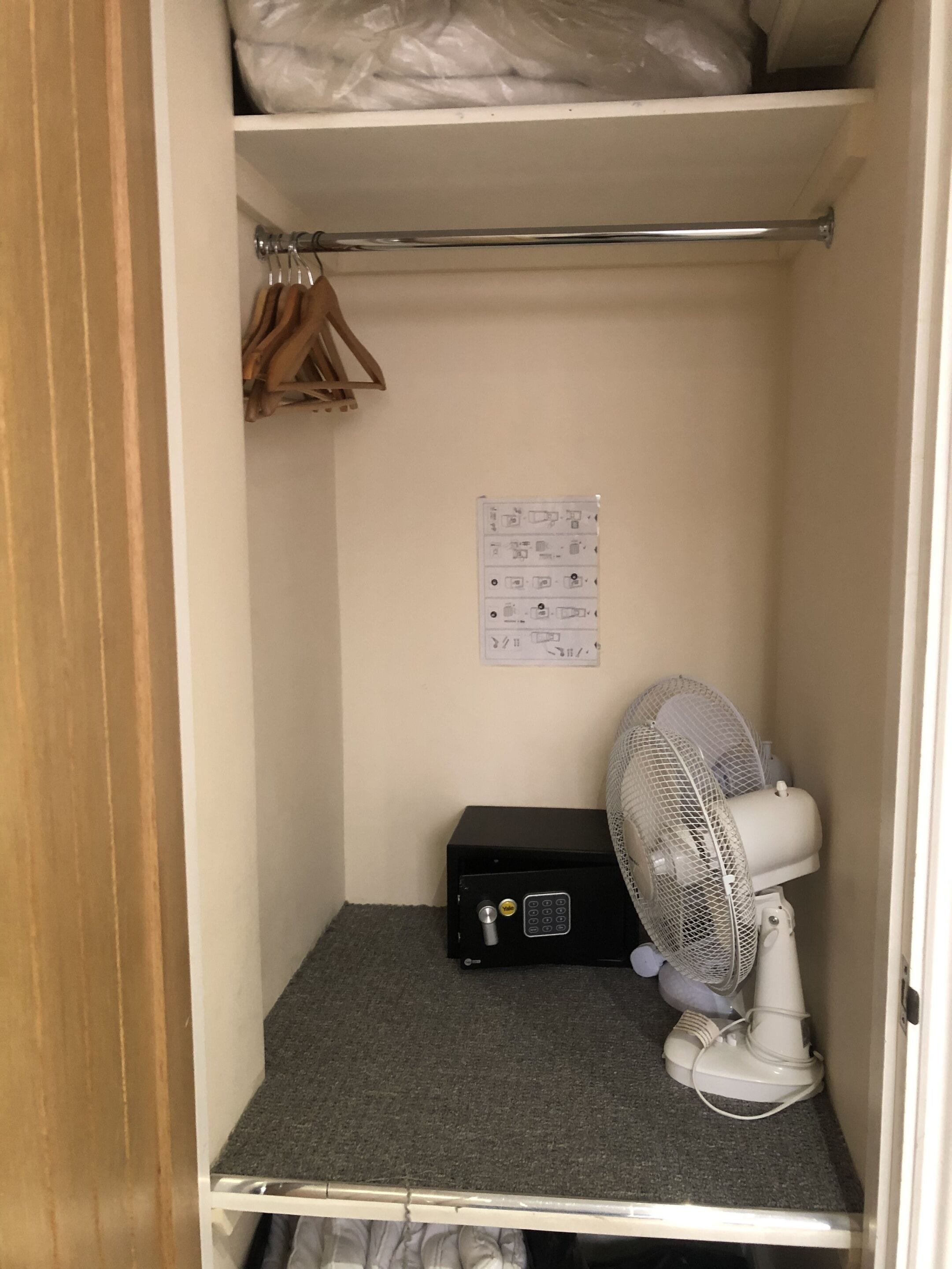 A small, enclosed room with a ceiling fan, a black safe, and a white wall with a power outlet.