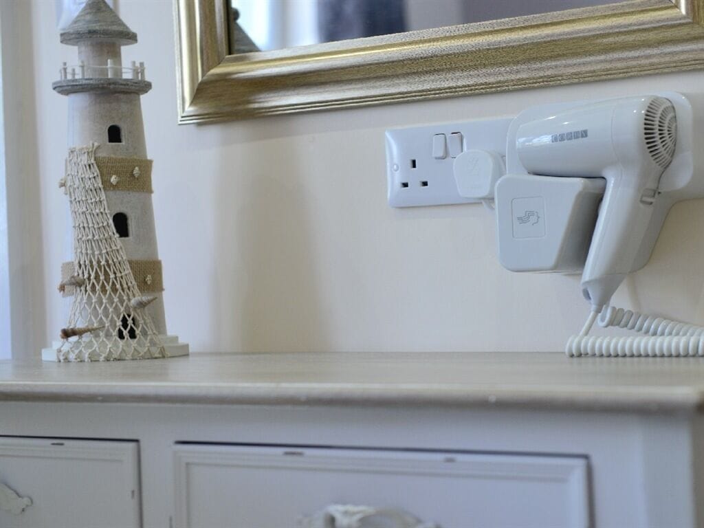 A white dresser with a small lighthouse model, a hairdryer, and a power outlet.