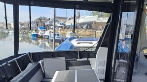 Interior de un barco con zona de estar, una mesa y vistas al puerto deportivo.