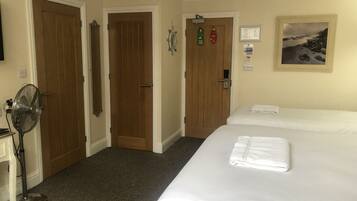 A hotel room with two beds, a fan, and a painting on the wall.