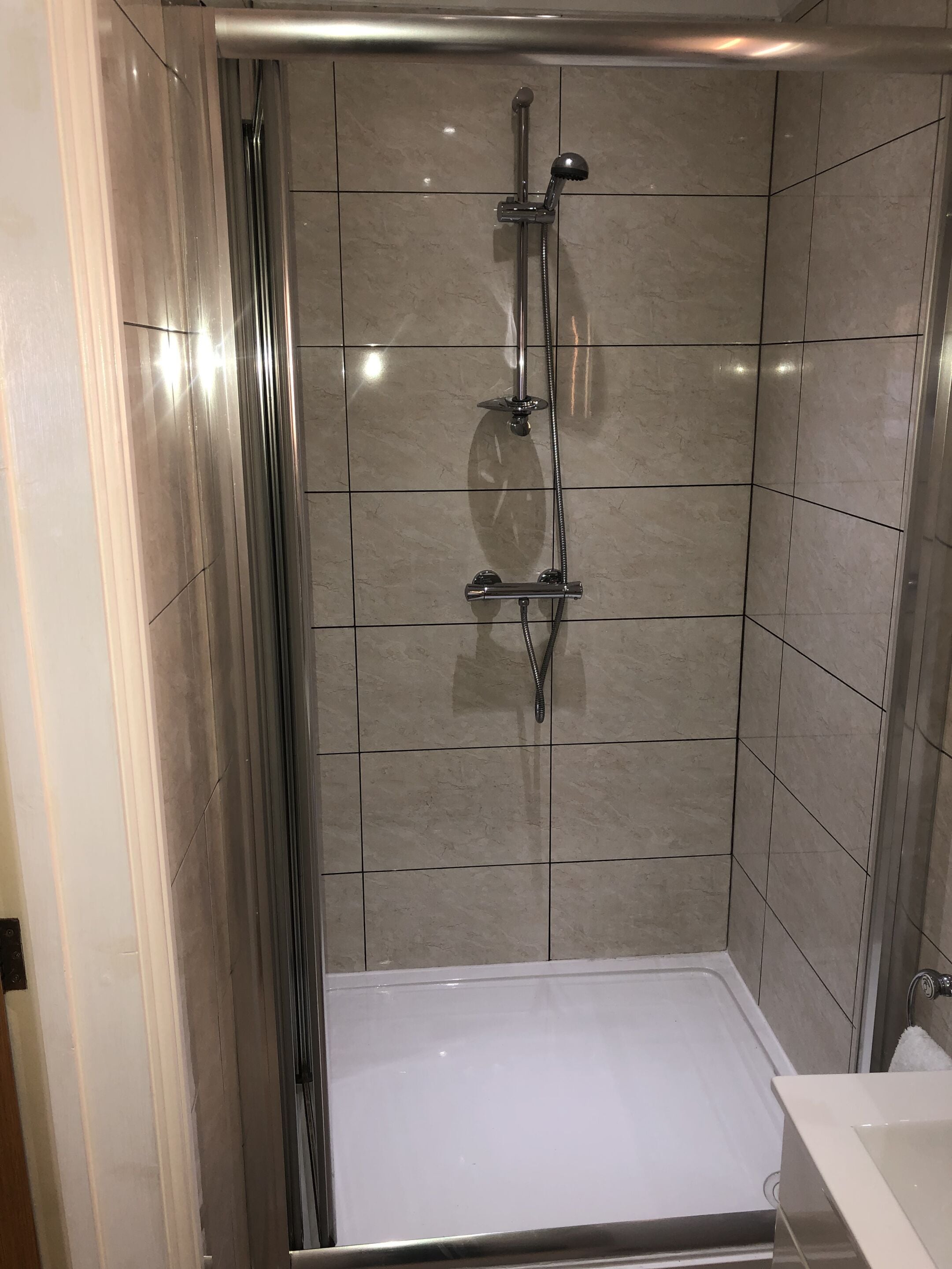 Un espace douche moderne doté d’une porte en verre, d’un pommeau de douche à main et d’un pommeau de douche fixe.