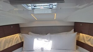 Una cabaña compacta y bien iluminada con una cama individual, una toalla doblada con cuidado, un ventanal pequeño y un cabecero con luz integrada.