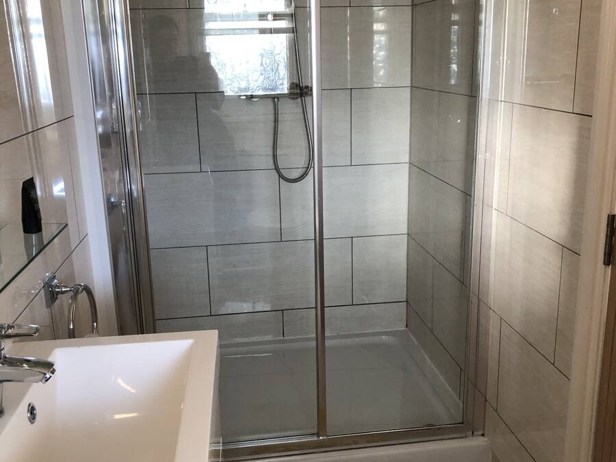 Un baño moderno con ducha de vidrio, un lavamanos blanco y un tapete de toalla con la palabra 'Soda'.