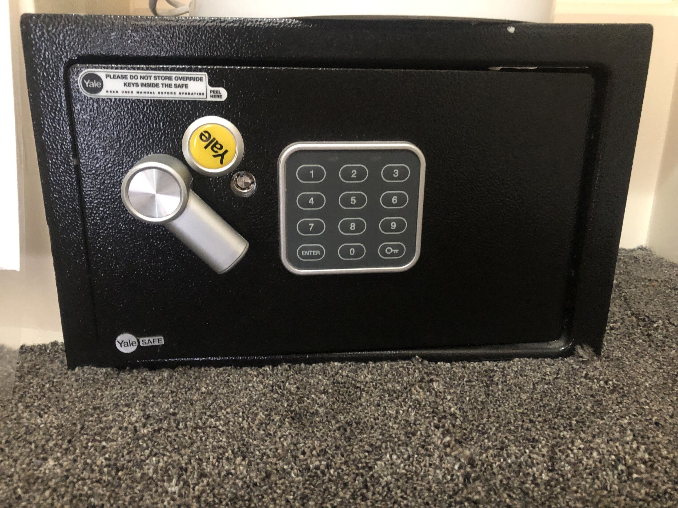 A black safe with a Yale lock, a numeric keypad, and a keyhole.