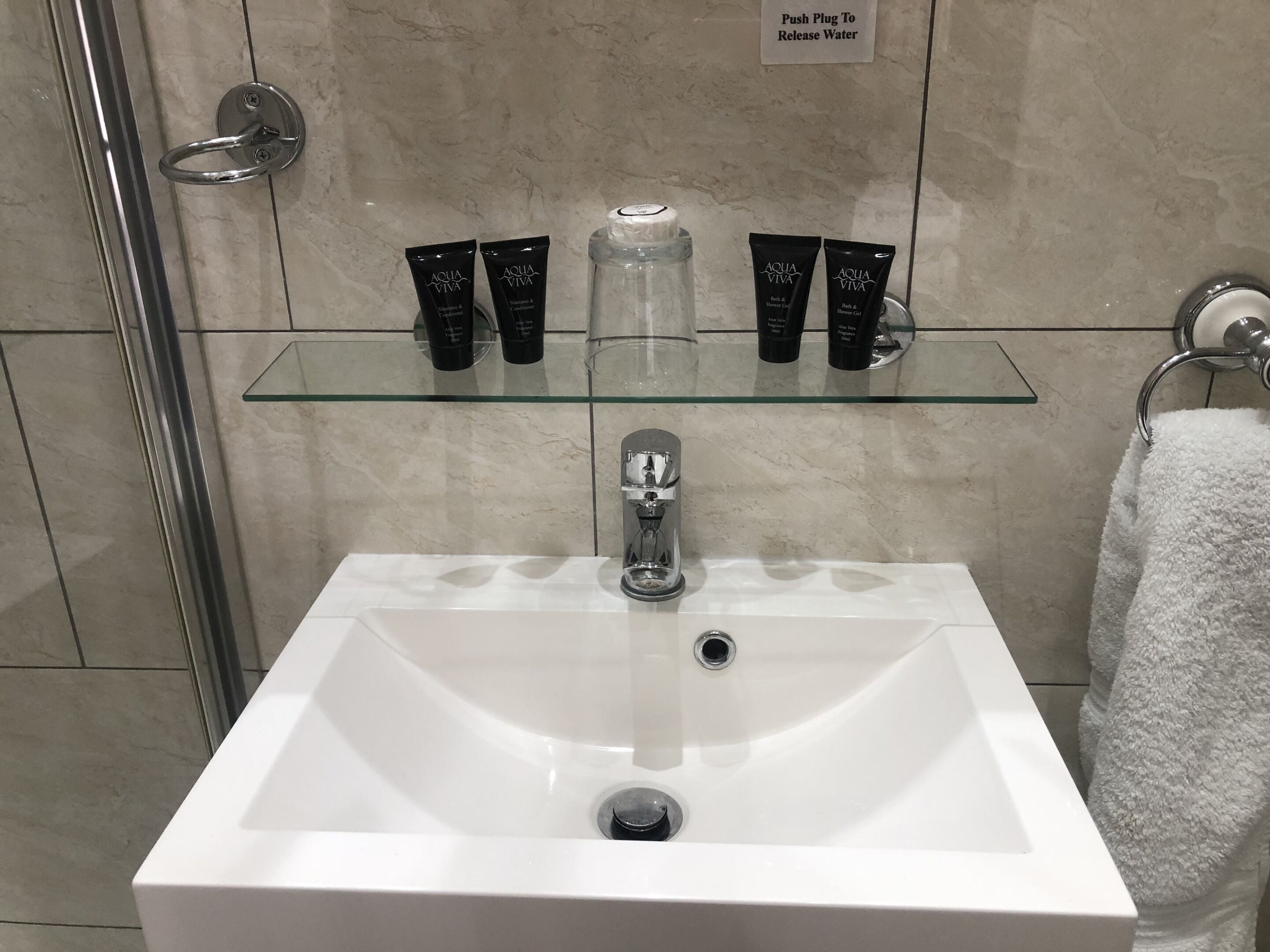 A bathroom with a white sink, glass shelves holding toiletries, a glass shower enclosure, and a towel rack.