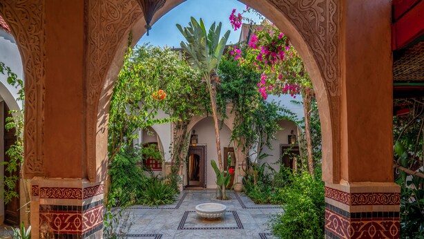 An ornate courtyard with a tiled floor, archways, and lush greenery.
