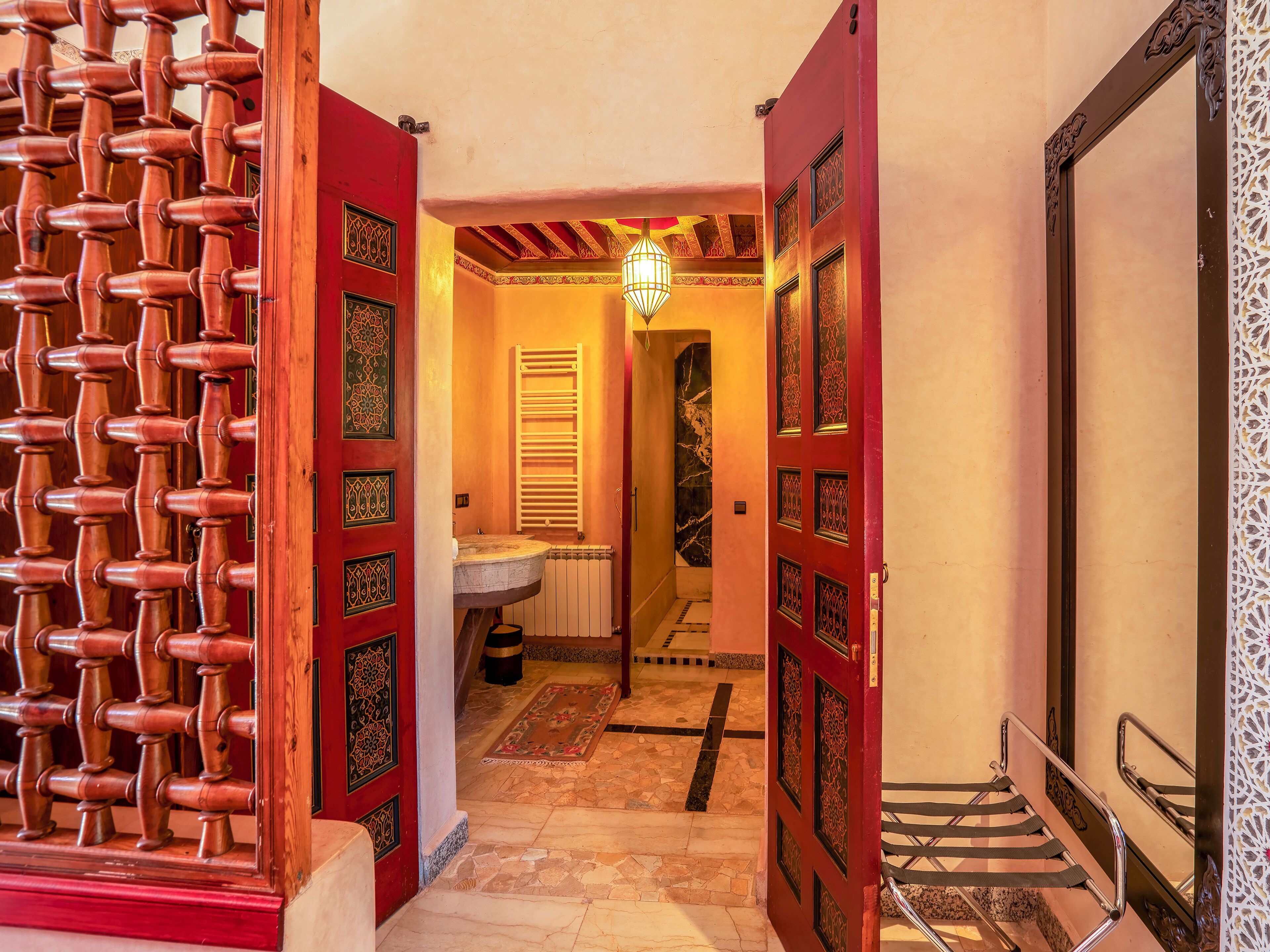 Um corredor com portas de madeira ornamentadas, piso ladrilhado e luminária pendente.