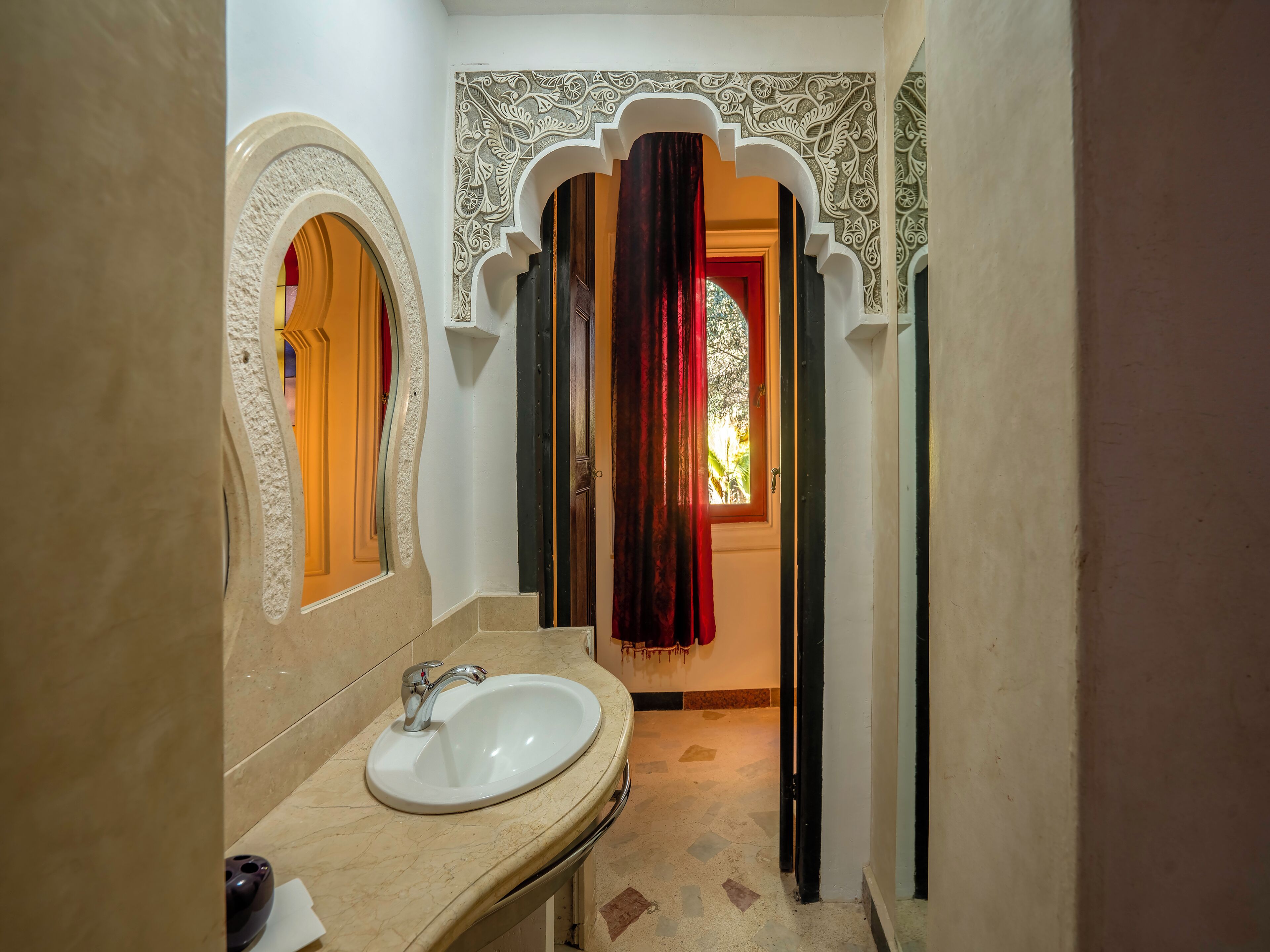 Une salle de bain avec un lavabo blanc, un miroir et une porte donnant sur une autre pièce.