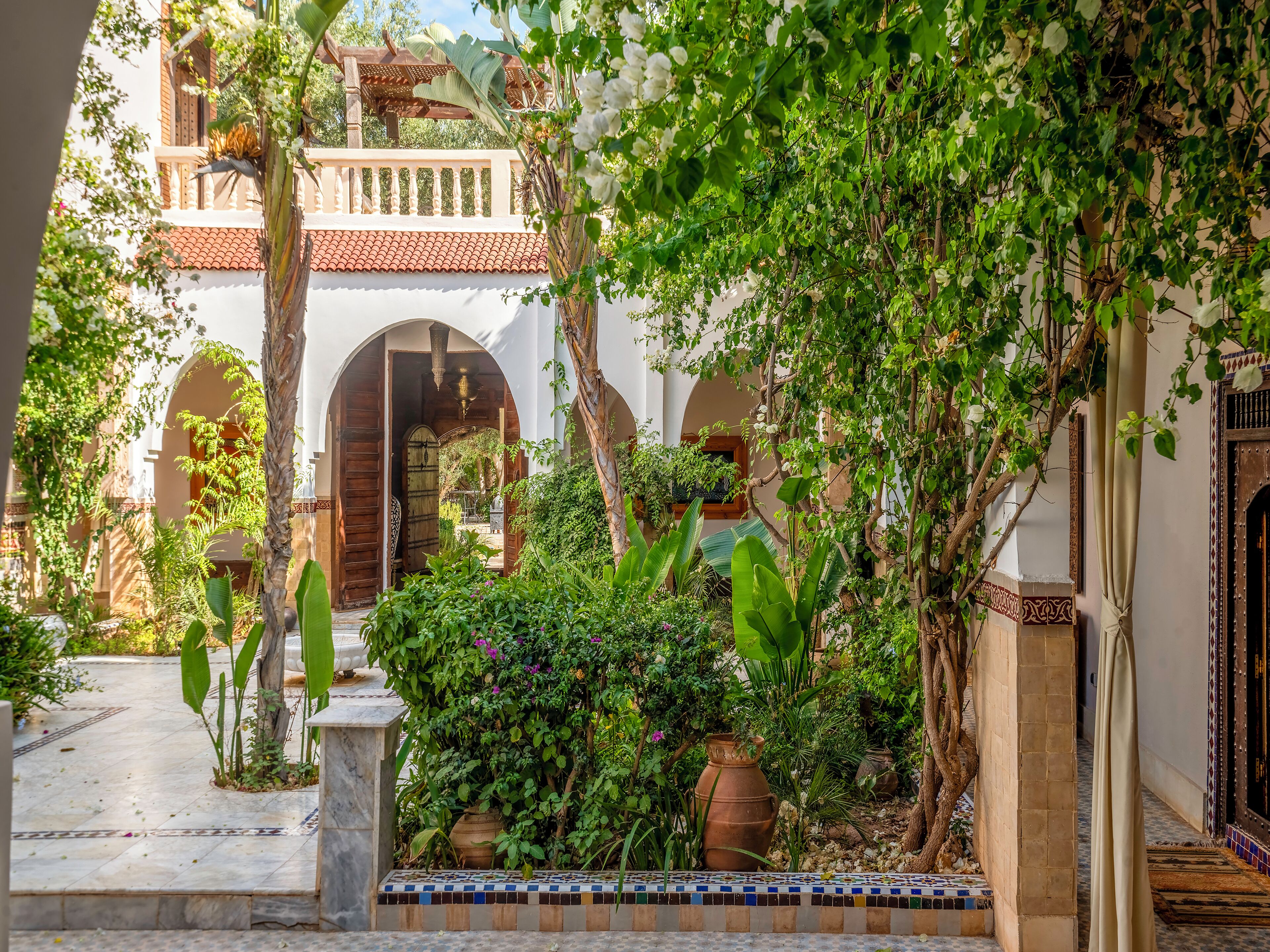 Un patio con arcos, suelo de baldosas y abundante vegetación.