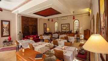 Un comedor con mesas dispuestas para los huéspedes, un mostrador de recepción de madera y un gran jarrón decorativo.