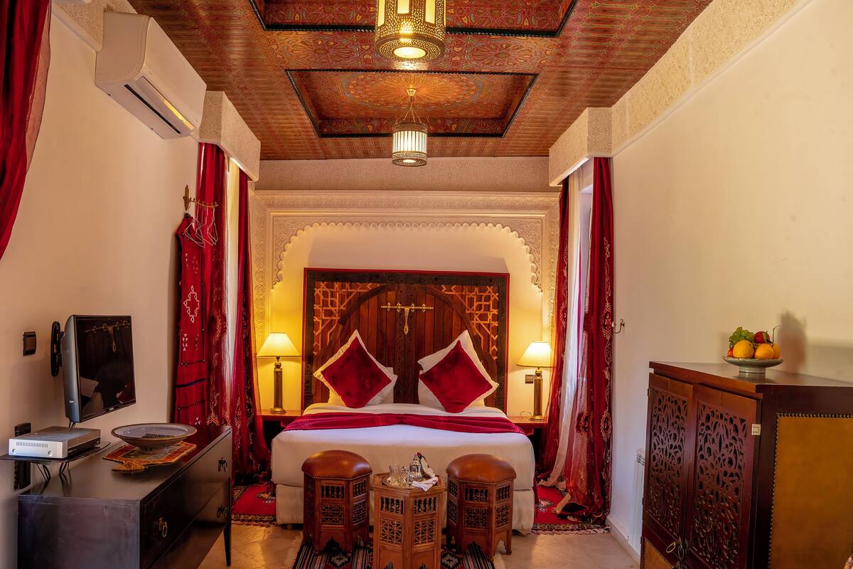 A traditional room with a bed, two bedside tables, a TV, and a decorative cabinet.