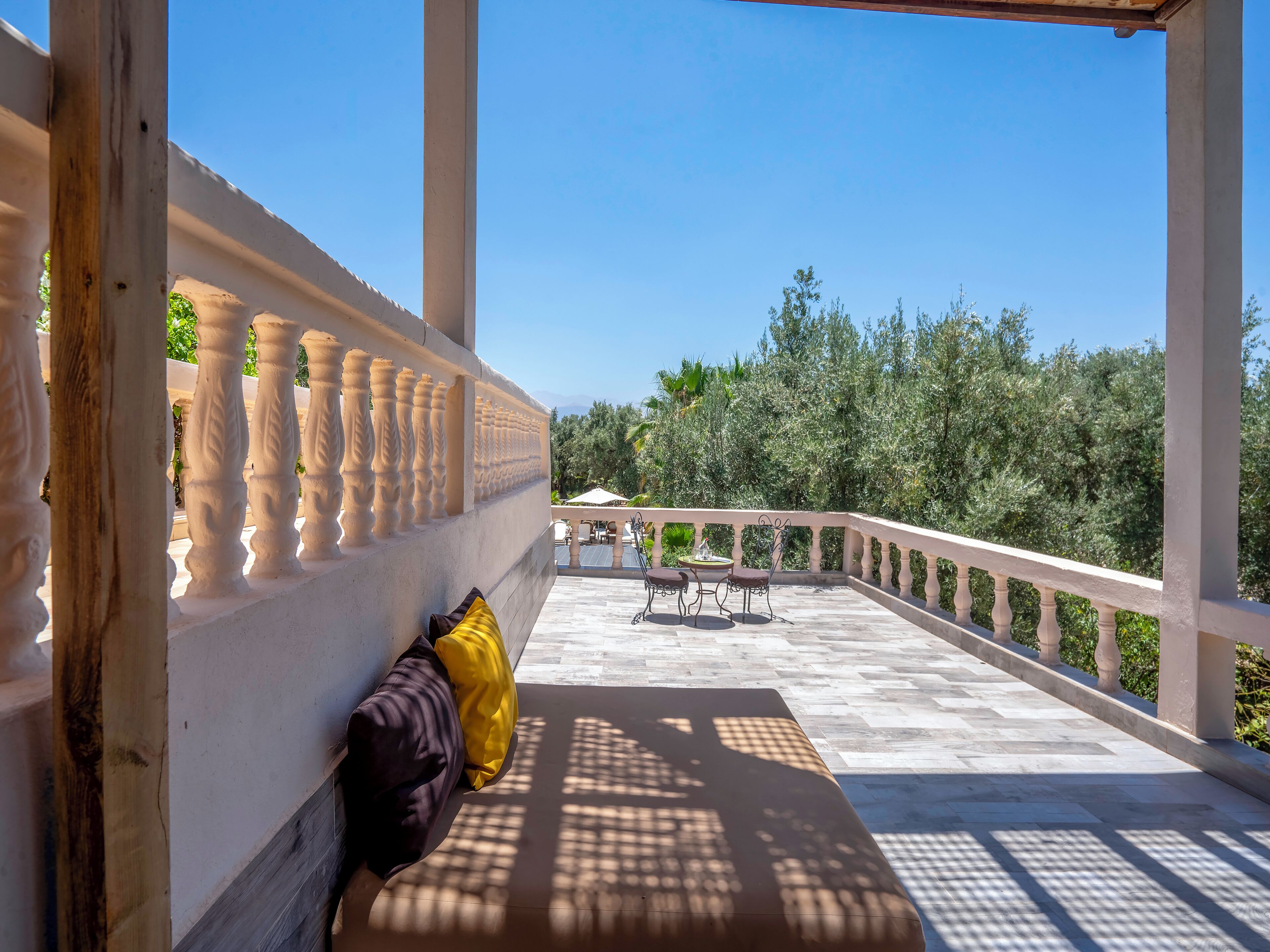 Ein Balkon mit weißer Brüstung, einer Bank mit Kissen und einem Tisch mit Stühlen.