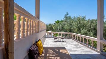 Ein Balkon mit weißer Brüstung, einer Bank mit Kissen und einem Tisch mit Stühlen.