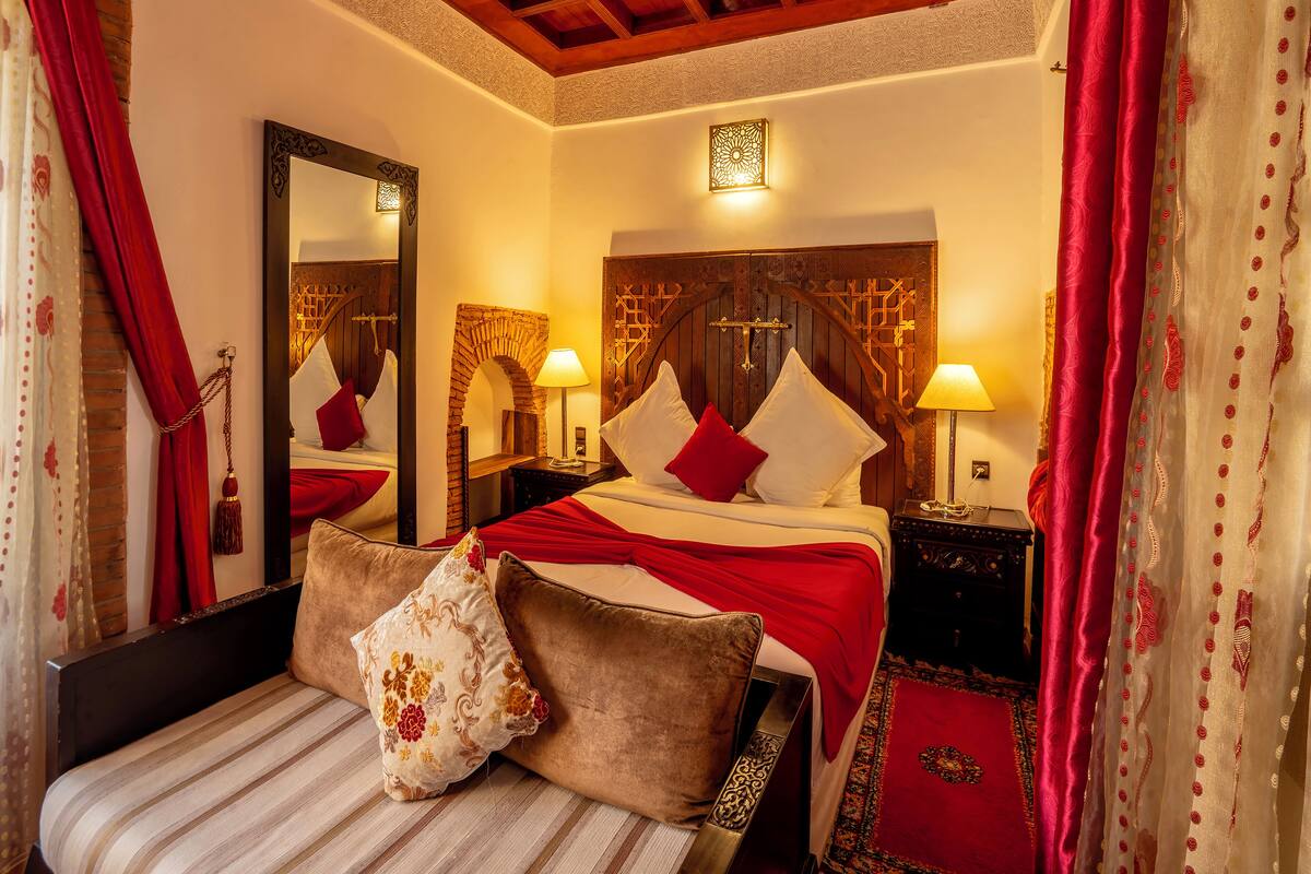 A hotel room with a large bed, two bedside tables, a mirror, and a red and white patterned curtain.
