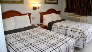 A hotel room with two beds, each with a checkered bedspread, a wooden headboard, and a nightstand with a lamp.