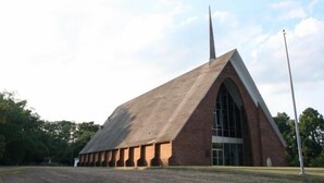 A large, modern building with a prominent triangular roof and a tall spire.