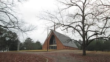 A building with a triangular roof and large windows, surrounded by trees and a leaf-covered ground.