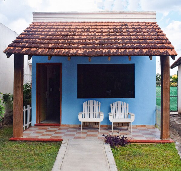Una pequeña construcción con techo de tejas, dos sillas blancas y una pantalla negra grande.