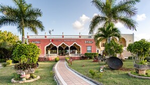 Un bâtiment à la façade rouge, doté d’une entrée couverte et d’une enseigne indiquant : « Capital O Hacienda Sanchinez Restaurant ».