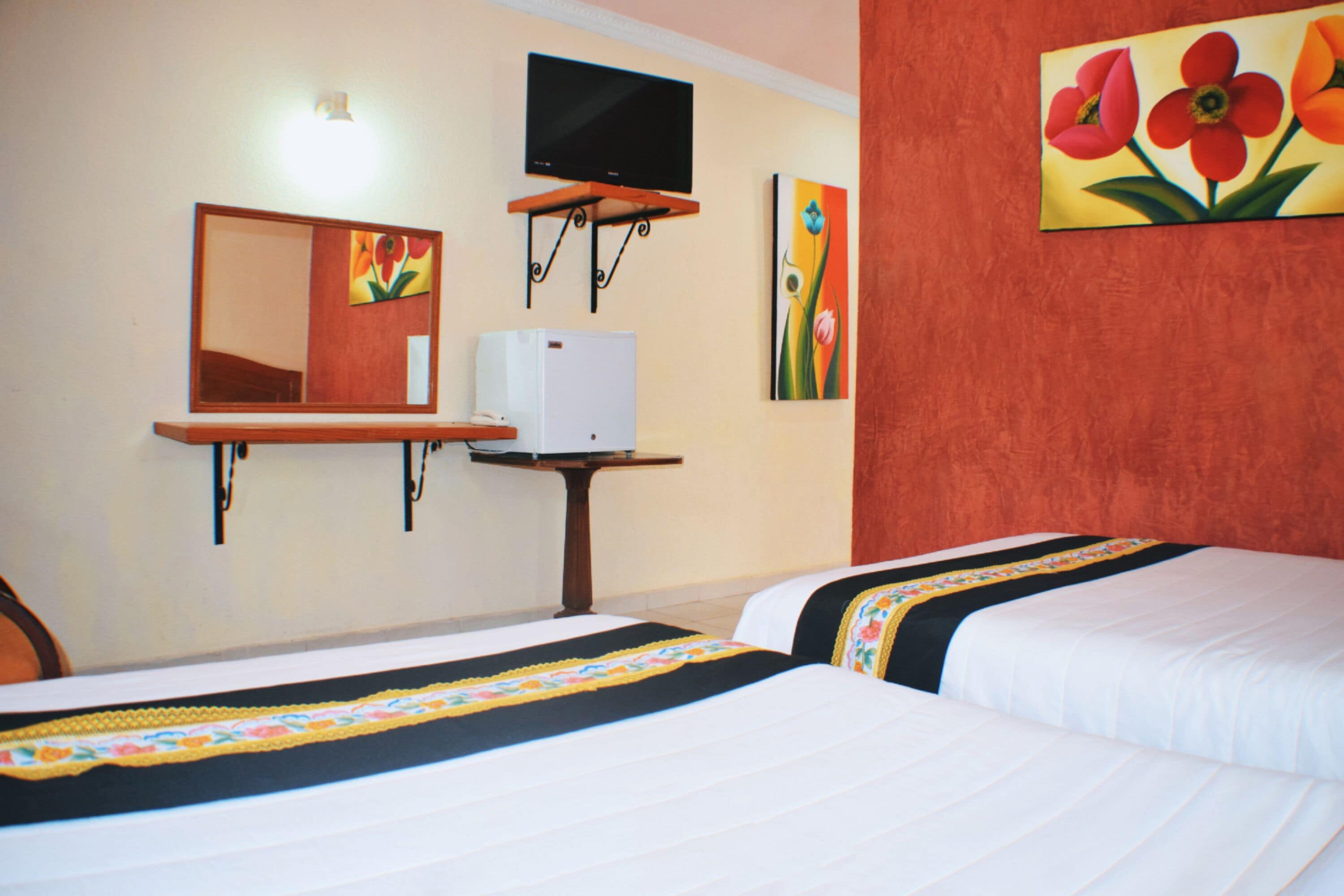 A hotel room with two beds, a television mounted on the wall, a small table, and artwork on the walls.